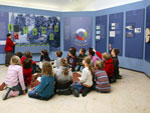 Bild vergrößert sich per Mausklick:Kindergruppe vor dem Ausstellungsensemble: Samenverbreitungsstrategien der Bäume)